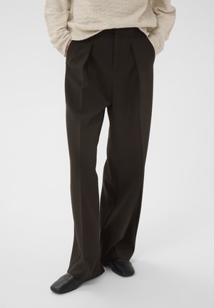 Beige long-sleeve sweater and loose black pleated trousers worn with black flat shoes on a person standing against a plain background.