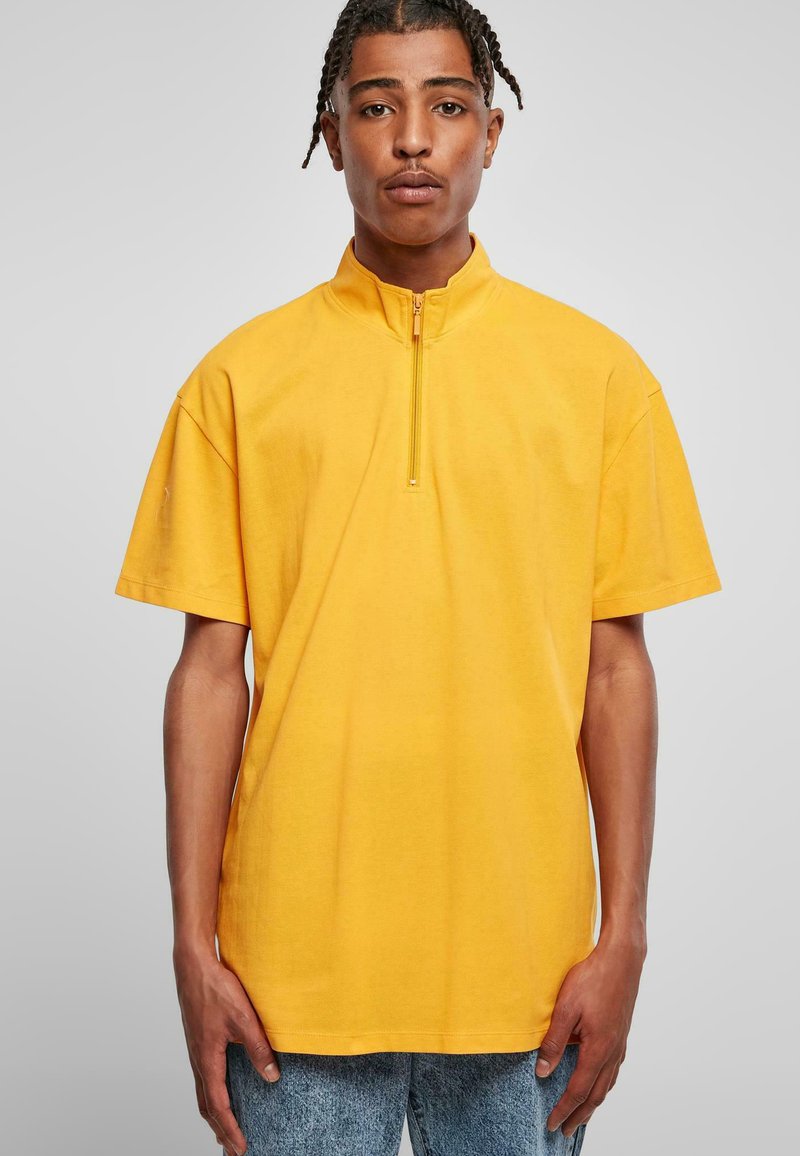 Yellow short-sleeve top with a high collar and half zip, featuring a smooth texture and a relaxed fit. Paired with light blue jeans.