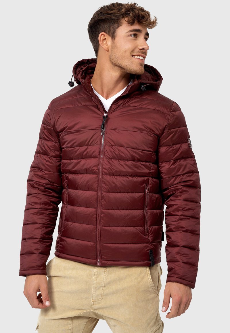 Jachetă puffer burgundy cu fermoar frontal, design matlasat și glugă. Dispune de două buzunare laterale și un logo pe mânecă.