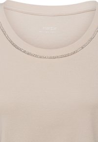 Beige top met ronde hals, versierd met een rij kleine zilveren kralen langs de kraag.