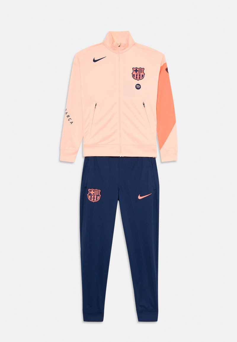 Tracksuit in light pink and navy blue. Jacket features high collar, zip pockets, and team logo. Pants have elastic cuffs and logo on leg.