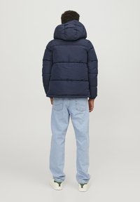 Mörkblå puffjacka med huva, kviltad design och elastiska ärmslut. Bärs med ljusblå jeans och vita sneakers.