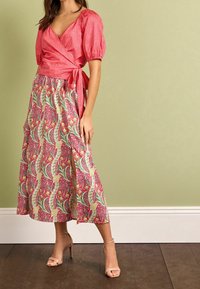 Top avvolgente rosa con maniche a sbuffo abbinato a una lunga gonna a fantasia con design floreale e uno spacco laterale. Tacchi beige completano il look.