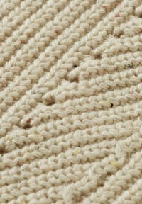 Tissu tricoté de couleur crème avec un motif texturé. Les fibres sont douces et épaisses, présentant des nuances subtiles pour plus de détails.