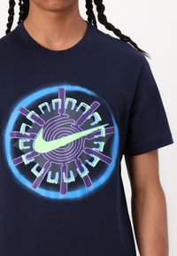 Mørkeblå bomulls T-skjorte med et sirkulært grafisk design som har en grønn Nike-logo, lilla detaljer og en lysende blå kant.