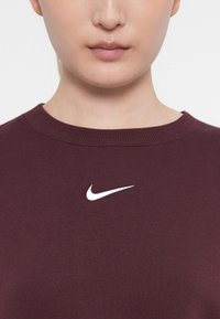 Μπορντό φούτερ φτιαγμένο από μαλακό ύφασμα, με στρογγυλή λαιμόκοψη και μικρό λευκό λογότυπο Nike στο στήθος. Λείο υλικό με ριμπέ λαιμό.