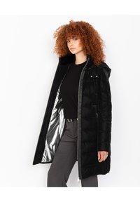 Chaqueta acolchada negra con capucha, con un forro plateado brillante, textura acolchada y cremallera frontal. Incluye detalle de bolsillo con solapa.