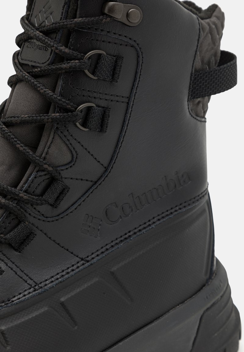 Botín impermeable negro con parte superior sintética texturizada, puntera reforzada y suela de goma texturizada. Presenta ojetes de metal y el logo de Columbia.