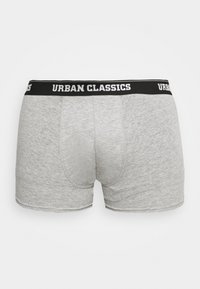 Sive pamukaste bokserice s crnim elastičnim pojasom na kojem piše "URBAN CLASSICS" u bijelom tekstu; glatka tekstura i prilagođen dizajn.