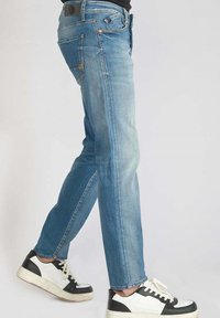 Jeans en denim bleu clair avec une coupe droite, design à cinq poches et légères déchirures. Portés avec des baskets noir et blanc.