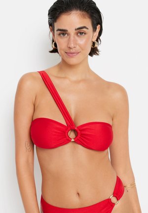 Rdeča bikini zgornji del z zvitim dizajnom in okrožnim zlatim okrasjem na sredini. Ena naramnica je široka, medtem ko druge ni.