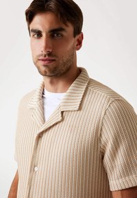 Short-sleeve shirt made of textured fabric in beige with white horizontal stripes, featuring a pointed collar and button closure.