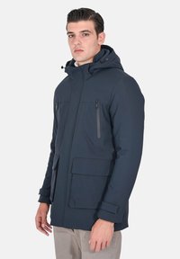 Giacca impermeabile blu navy con cappuccio, dotata di due tasche con zip sul petto e una grande tasca anteriore, realizzata in tessuto liscio e resistente.