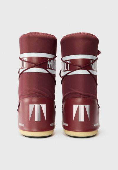 Botas lunares de nylon rojo y goma con parte superior acolchada, marca blanca y suela texturizada. Presentan correas entrelazadas y puntas redondeadas.