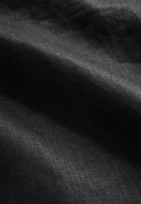 Gros plan sur un tissu noir avec une texture de tissage visible et des plis doux créant des ombres douces.