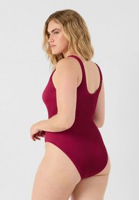Bañador de una pieza burdeos con relieve, con tirantes anchos, espalda en forma de u y cortes altos en las piernas, que exhibe un diseño de tejido texturizado.