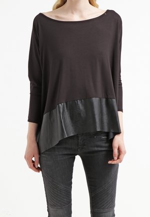 Top nero a maniche lunghe con scollo a U, caratterizzato da un pannello inferiore in similpelle. Abbinato a jeans aderenti grigio scuro con texture.