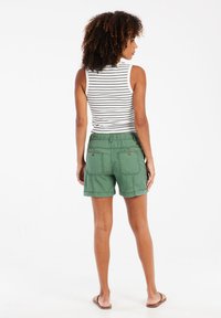 Groene katoenen shorts met een casual ontwerp, elastische tailleband en opgerolde hems. De persoon draagt een gestreept tanktop en sandaaltjes.