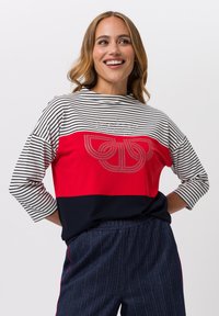 Gestreifte Langarmbluse mit roten und schwarzen Farbkblocks, einer dekorativen Grafik und einem runden Ausschnitt. Der Stoff hat eine glatte Textur.