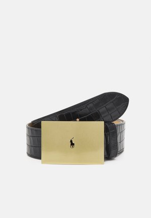 Ceinture en cuir noir texturé, roulée, avec une grande boucle rectangulaire dorée présentant un petit logo noir de joueur de polo en son centre.
