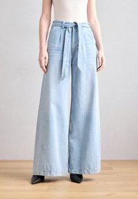 Světlé modré široké džíny s vysokým pasem a zavazovacími pásky. Vyrobeno z denimu, s plisovaným designem a jemnou texturou.