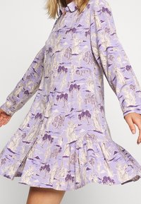 Robe lilas légère ornée d'un imprimé fantaisiste de personnages et d'arbres, avec un col à boutons et un ourlet volanté évasé. Manches longues.
