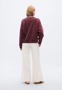 Μακρυμάνικο πουλόβερ σε βυσσινί με στρογγυλή λαιμόκοψη και χαλαρές ραφές στους ώμους, σε συνδυασμό με άσπρο παντελόνι υψηλής μέσης και φαρδιάς γραμμής. Απαλό ύφασμα.