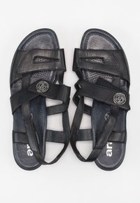 Schwarze Ledersandalen med flera remmar och en cirkulär metallaccent. Texturerade innersulor och ergonomisk design för komfort. Ovanifrån.