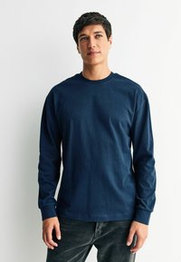 Námořnické tričko s dlouhým rukávem vyrobené z měkké látky, s kulatým výstřihem, volným střihem a žebrovanými manžetami. Kombinováno s tmavými džínami.