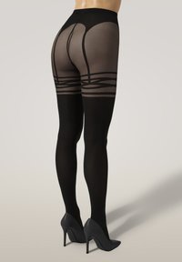 Kvinna i svarta mönstrade genomskinliga strumpbyxor och svarta högklackade skor, visad bakifrån mot en enfärgad bakgrund.