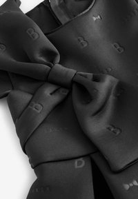 Vestido de satén negro con detalle de lazo, logotipos en relieve "B" y "BAKER", textura suave y un diseño de drapeado elegante.