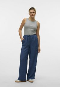 Grijze mouwloze top met geribbelde textuur, gecombineerd met loszittende, donkerblauwe broek met trekkoord en twee voorzakken.
