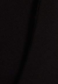 Gros plan sur un tissu noir montrant une texture tissée fine et un détail de couture verticale.