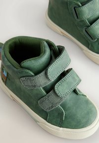 Rohelised nahast kõrgema säärega kingad, millel on kaks reguleeritavat VELCRO rihma, tekstureeritud pind ja valged kummist tallad kerge mustriga.