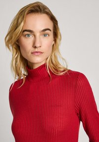 Top de cuello alto de canalé rojo con un diseño ajustado, tejido texturizado y un sutil detalle del logo en el pecho.