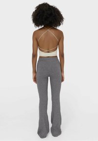 Kremowy, prążkowany crop top z krzyżującymi się ramiączkami na plecach, zestawiony z szarymi, prążkowanymi spodniami flare. Gładka tekstura materiału, dopasowany krój.