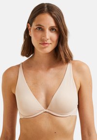 Soutien-gorge triangulaire beige clair avec des bretelles fines, en tissu lisse, et une couture frontale torsadée. Design simple sans matériel ou motifs visibles.