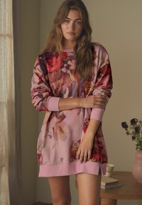 Sweatshirtová šaty s kvetinovým vzorom v ružových odtieňoch, so širokým rebrovaným výstrihom a manžetami, vyrobené z jemnej štruktúrovanej látky.