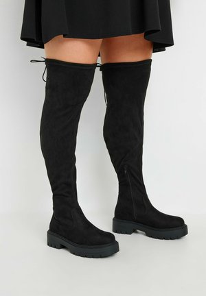 Zwarte over-de-knie laarzen gemaakt van zachte suede, met een dikke zwarte rubberen zool, een zijrits en verstelbare veters aan de bovenkant.