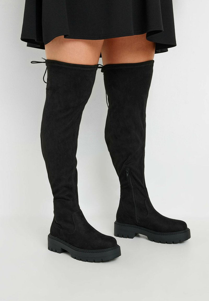 Svarta knähöga stövlar i mjukt mocka, med en tjock svart gummisula, sidodragkedja och justerbara snören upptill.