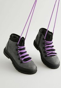 Bottes de randonnée en suede gris avec un col noir, dotées de lacets en corde violette, d'œillets en métal et d'une fermeture éclair sur le côté. Semelle texturée pour une meilleure traction.
