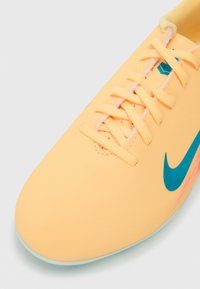 Zbliżenie na żółty but sportowy z sznurówkami i niebieskim logo Nike na białym tle.