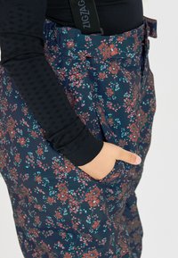 Blommiga byxor med marinblå bas, med ett flerfärgat blommönster, en elastisk midja och sidofickor. En strukturerad svart topp syns.