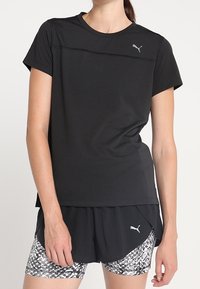 Černé sportovní tričko s krátkým rukávem, kulatým výstřihem a šitými detaily. V kombinaci s šortkami s černobílým vzorem, které mají logo.