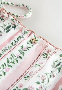 Țesătură cu model floral, având frunze verzi și flori roz, cu dungi roz cu margini ondulate. Accente din metal auriu afișate.