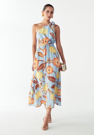 Robe longue fleurie en tissu bleu clair avec des fleurs orange et jaunes. Le modèle asymétrique à une épaule présente une taille froncée et une jupe fluide.