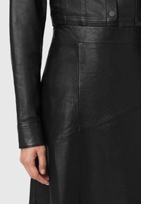 Sort læderkjole med figursyet design og glat tekstur. Den har en taljesøm og lagdelte detaljer. Manchetterne har en let glans og syning.