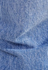 Blå denimtyg med en slät yta och ett subtilt, varierat mönster. Materialet visar små variationer i nyans och väv.