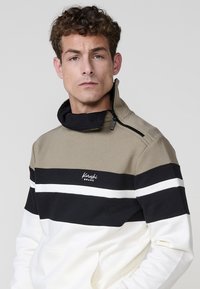 Khaki, čierny a biely dvojfarebný sweatshirt s vysokým golierom, zipsom a logom na hrudi. Bavlnený materiál, neformálny dizajn.