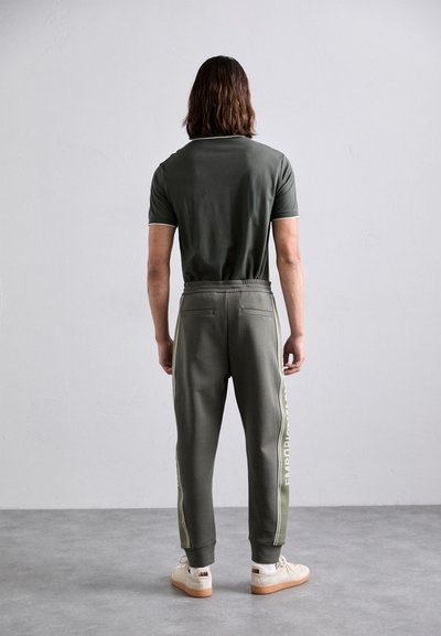 Olívovo zelený športový outfit pozostávajúci z priliehavého polo trička a zúžených teplákov so bočnými pruhmi a detailom loga. Štruktúrovaná tkanina a elastický pás.